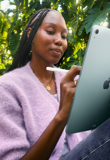 Một sinh viên đang ngồi bên ngoài. Cô ấy đang cầm iPad và Apple Pencil Pro.